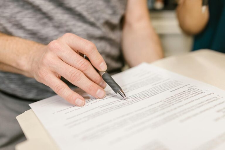 Close-up of a person's hand signing an important legal document with a pen indoors.